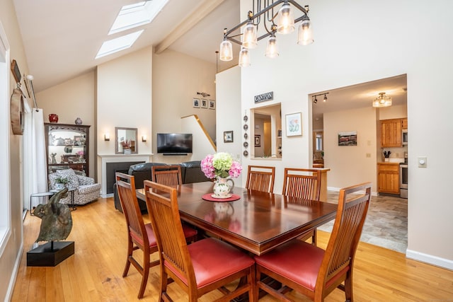 dining area with baseboards, high vaulted ceiling, a skylight, and light wood-style flooring
