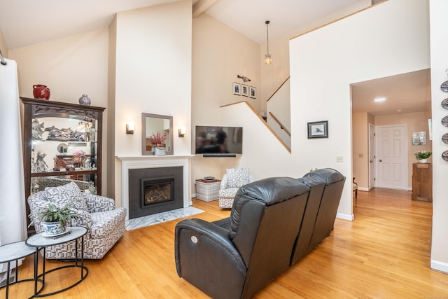 living room with a fireplace with flush hearth, beam ceiling, high vaulted ceiling, stairs, and light wood-style flooring