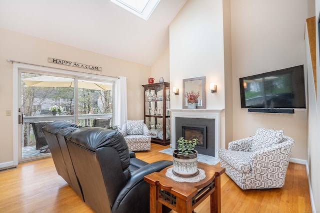 living area featuring visible vents, a skylight, a fireplace with flush hearth, high vaulted ceiling, and light wood-style floors