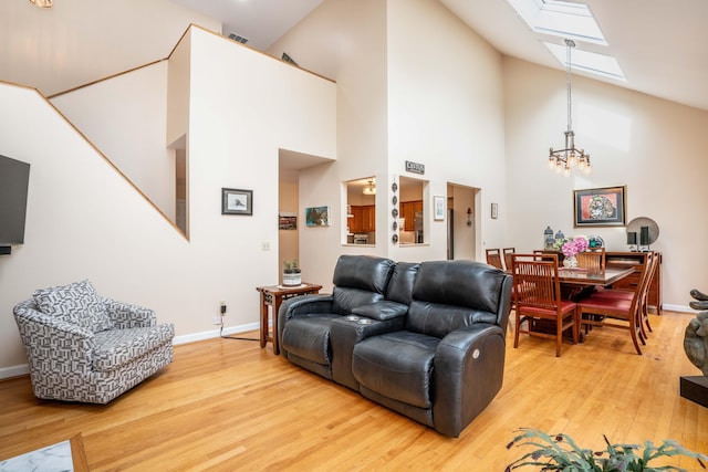 living area featuring a skylight, baseboards, high vaulted ceiling, and light wood-style floors