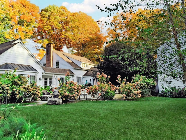 back of property featuring a standing seam roof, a chimney, and a yard