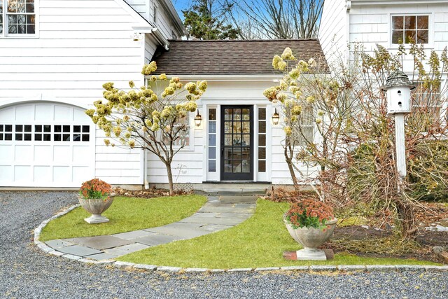 entrance to property with driveway, roof with shingles, and a garage