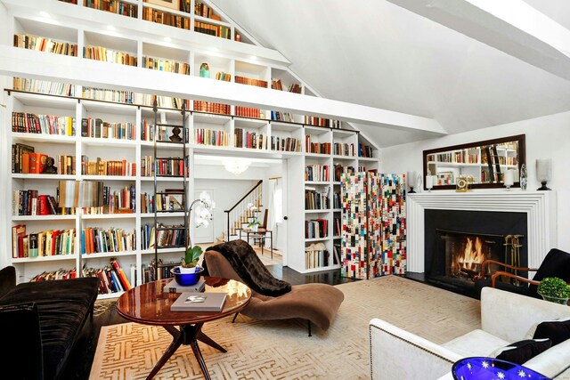 living area featuring a fireplace with flush hearth, stairs, and lofted ceiling
