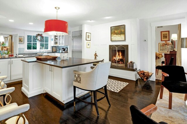 kitchen with dark countertops, stainless steel built in refrigerator, white cabinetry, and dark wood-type flooring