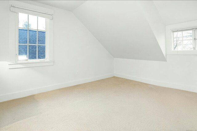 additional living space featuring light colored carpet, baseboards, vaulted ceiling, and a wealth of natural light