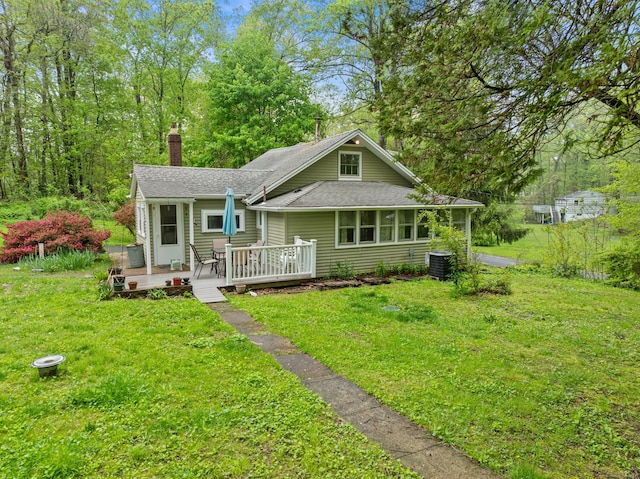 view of front of house featuring a chimney, a wooden deck, a front yard, and roof with shingles