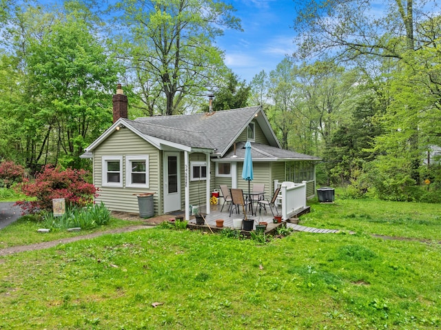 view of front facade with roof with shingles, a chimney, a front lawn, and a deck