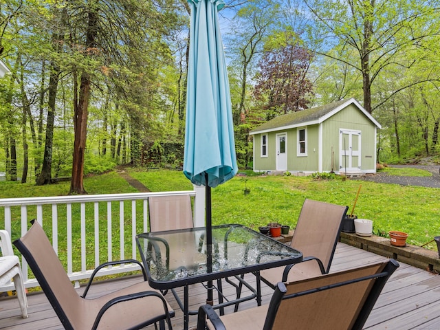 wooden terrace featuring outdoor dining space, an outbuilding, and a lawn