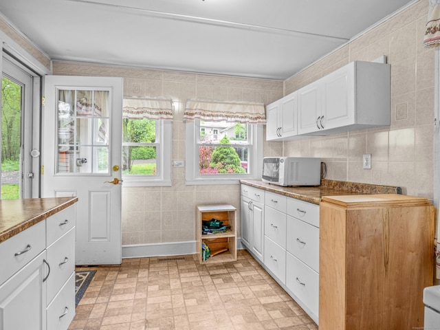 kitchen with white microwave, tile walls, white cabinets, and brick patterned floors