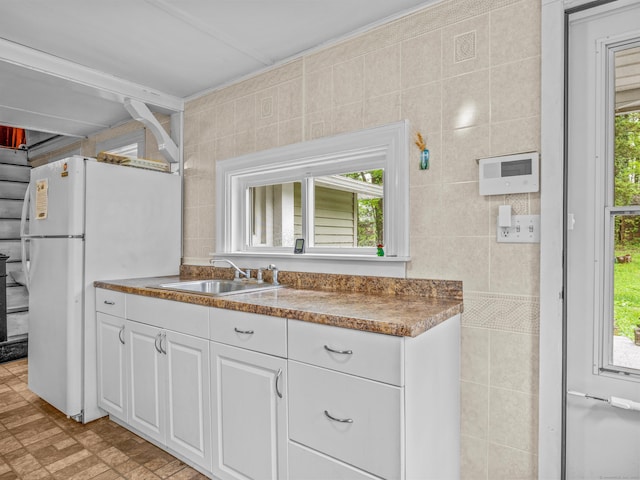 kitchen featuring a sink, plenty of natural light, white cabinetry, tile walls, and freestanding refrigerator