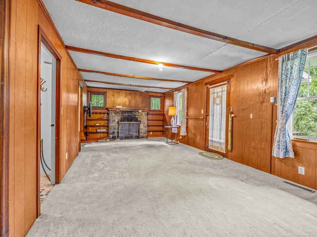 unfurnished living room with wood walls, a stone fireplace, carpet flooring, a textured ceiling, and beamed ceiling