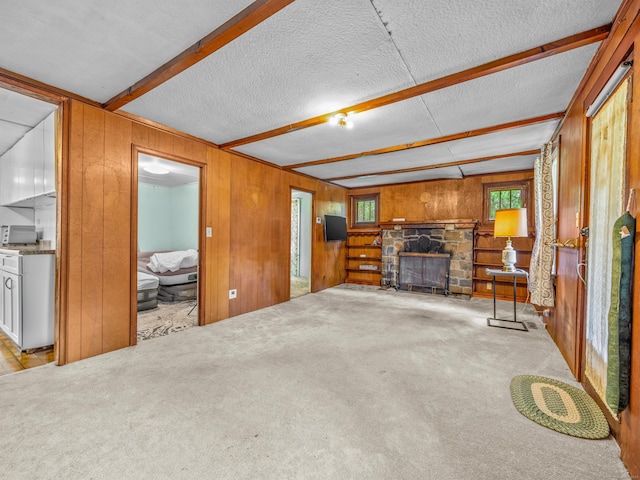 unfurnished living room featuring wood walls, carpet, a stone fireplace, and beamed ceiling