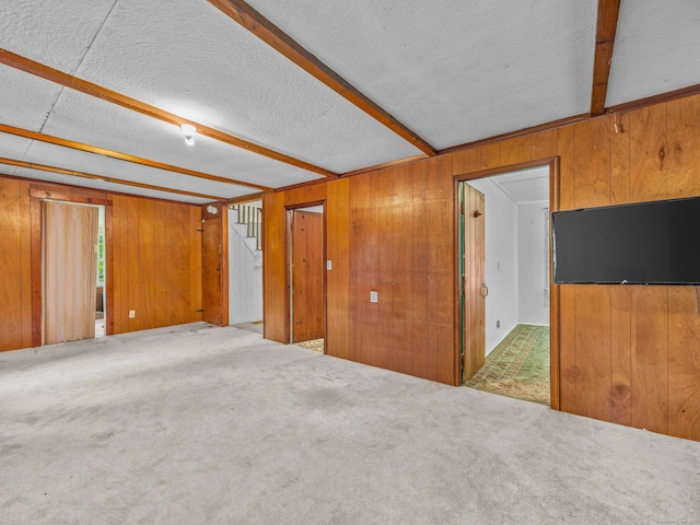 carpeted empty room featuring wood walls and beam ceiling