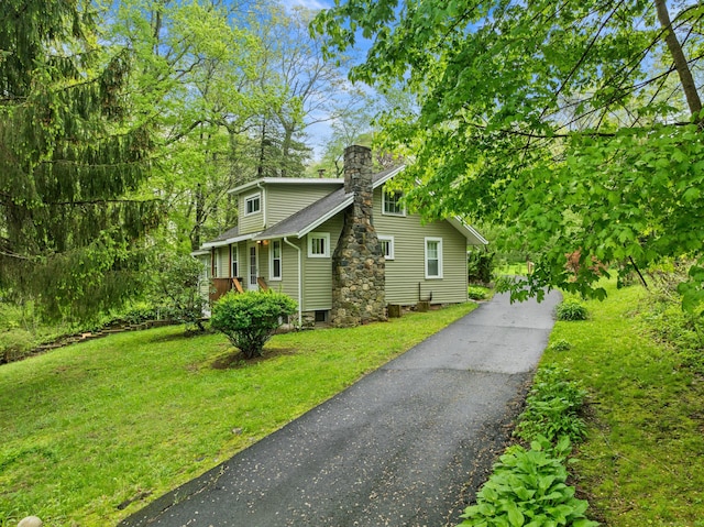 view of property exterior featuring a chimney, a lawn, and asphalt driveway