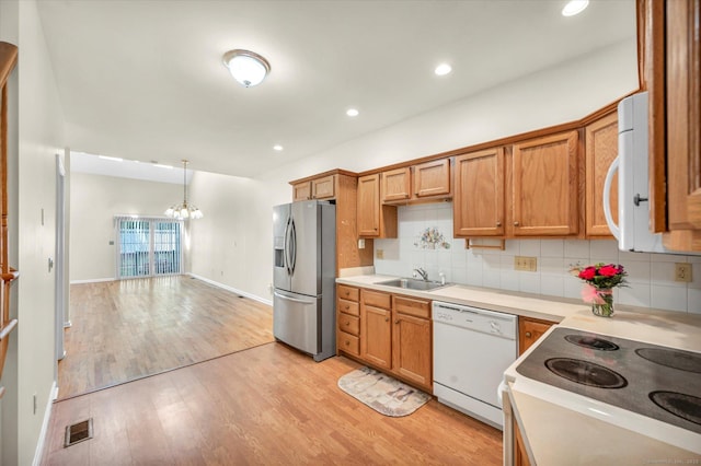 kitchen featuring white appliances, a sink, a chandelier, light wood finished floors, and light countertops