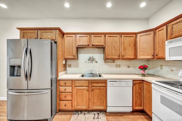 kitchen featuring white appliances, a sink, light wood finished floors, tasteful backsplash, and light countertops