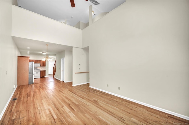 unfurnished living room featuring baseboards, a chandelier, light wood finished floors, and a ceiling fan