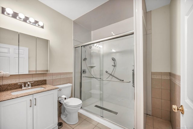 full bathroom featuring tile walls, tile patterned flooring, toilet, a stall shower, and a wainscoted wall