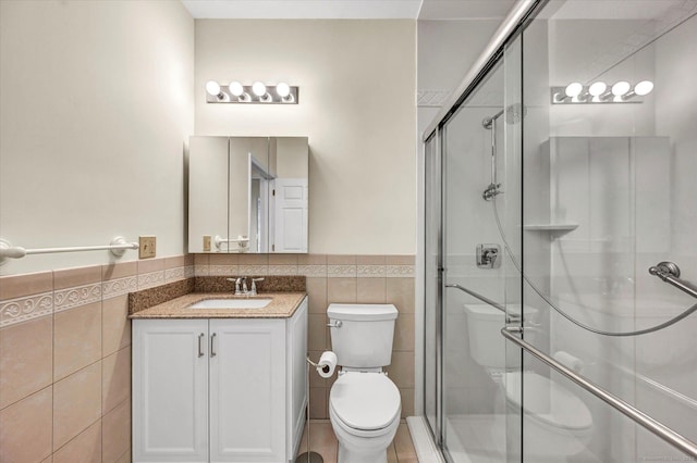 full bath with tile walls, toilet, a shower stall, a wainscoted wall, and vanity