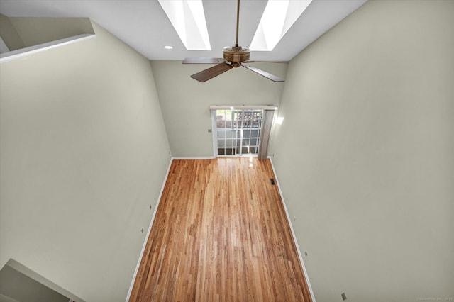 spare room featuring a skylight, a ceiling fan, baseboards, wood finished floors, and lofted ceiling
