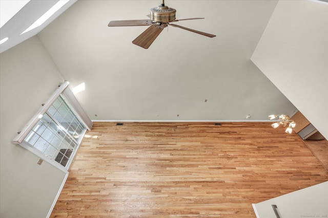unfurnished living room featuring wood finished floors, a ceiling fan, a high ceiling, baseboards, and a skylight