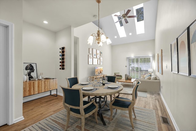 dining room featuring a skylight, wood finished floors, high vaulted ceiling, a chandelier, and baseboards