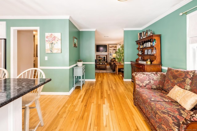 living area with crown molding, light wood-style flooring, baseboards, and a fireplace