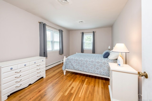 bedroom with light wood-style floors, a baseboard heating unit, and visible vents