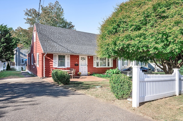 view of front facade with a shingled roof and fence