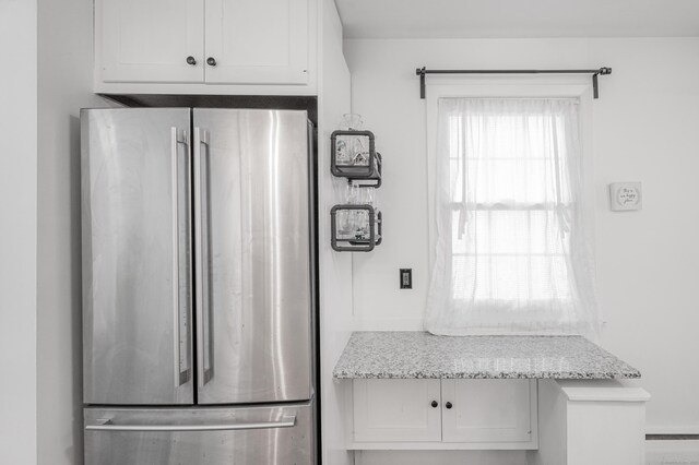 kitchen with freestanding refrigerator, white cabinetry, and light stone countertops