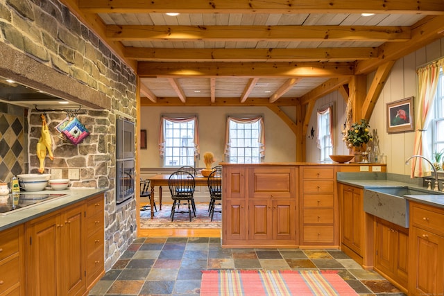 kitchen with wood ceiling, a sink, brown cabinetry, stone tile floors, and beamed ceiling