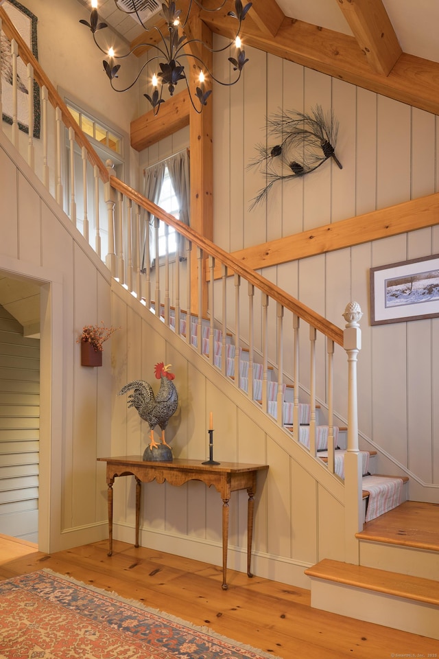 stairway with a notable chandelier, a decorative wall, a high ceiling, and hardwood / wood-style flooring