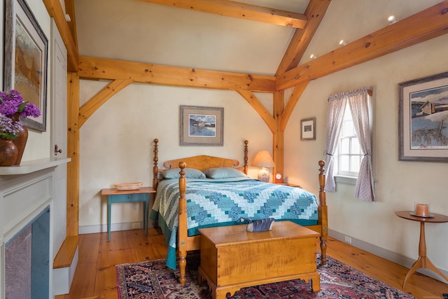 bedroom featuring baseboards, lofted ceiling with beams, hardwood / wood-style floors, and a fireplace