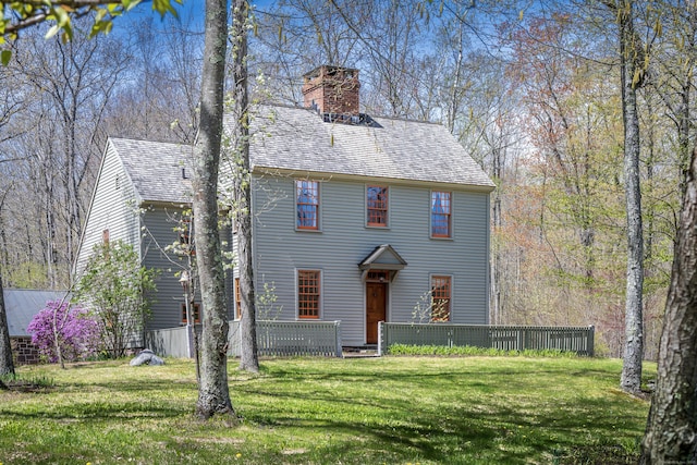 colonial home with a shingled roof, fence, a chimney, and a front yard