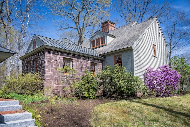 view of property exterior with a chimney, stone siding, a standing seam roof, and a lawn