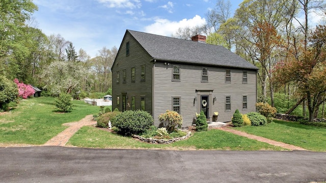 colonial-style house with a shingled roof, a chimney, and a front yard