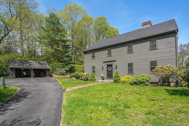 colonial house featuring roof with shingles, an outbuilding, a chimney, and a front yard