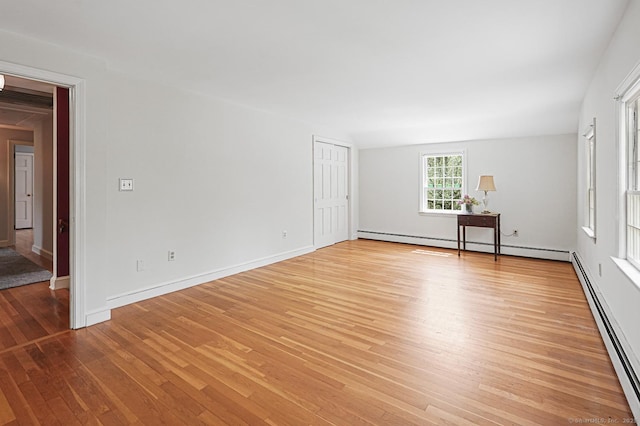 spare room featuring light wood finished floors, baseboards, and a baseboard heating unit