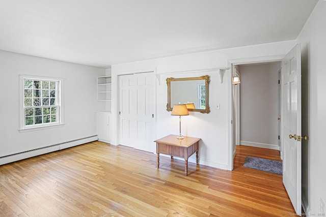 interior space featuring a baseboard radiator, baseboards, and light wood-style floors