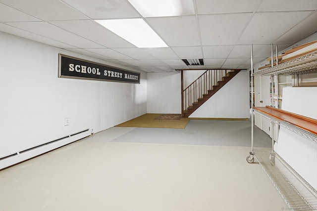 finished basement featuring a drop ceiling, baseboard heating, and stairs