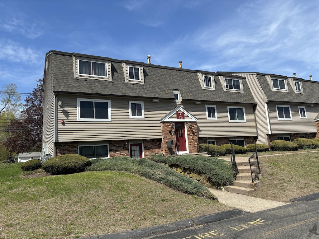 view of front facade featuring brick siding, mansard roof, a shingled roof, and a front lawn