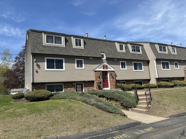 view of front facade featuring brick siding, mansard roof, a shingled roof, and a front lawn