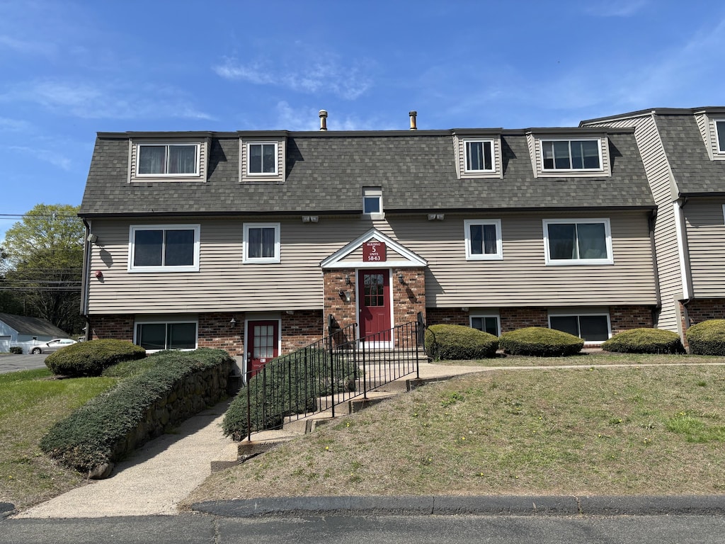 split foyer home featuring a shingled roof, mansard roof, brick siding, and a front yard