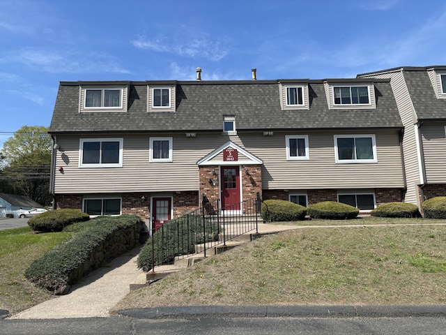 split foyer home featuring a shingled roof, mansard roof, brick siding, and a front yard