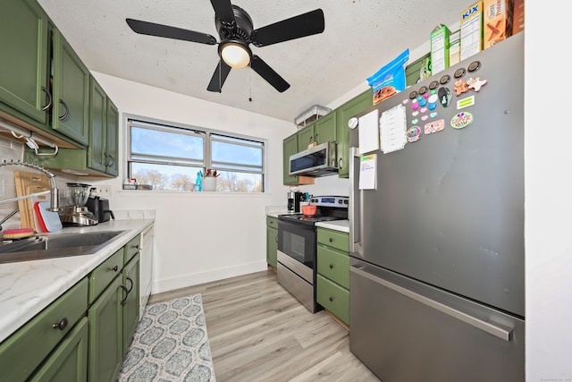 kitchen with light wood-style floors, light countertops, green cabinetry, a sink, and stainless steel appliances