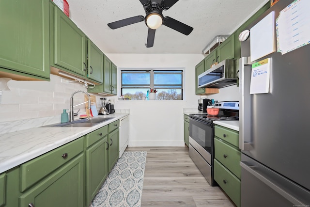 kitchen featuring light wood-type flooring, a sink, appliances with stainless steel finishes, backsplash, and green cabinets
