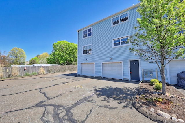 rear view of property featuring aphalt driveway, fence, and a garage
