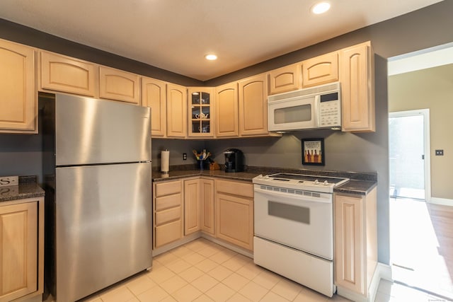 kitchen featuring white appliances, light brown cabinetry, and dark countertops