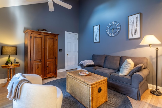 living area featuring a ceiling fan, a high ceiling, baseboards, and wood finished floors