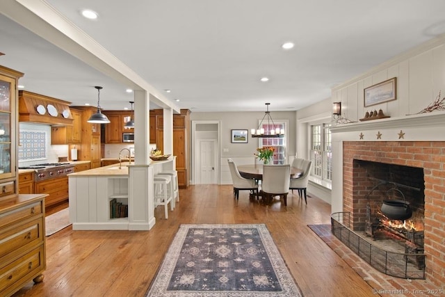 living area featuring a brick fireplace, light wood-style floors, recessed lighting, and a chandelier
